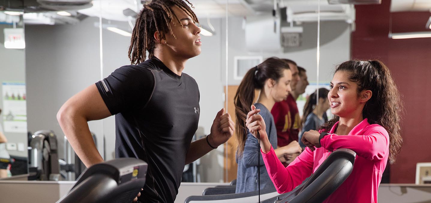 A student with a stopwatch observes a subject on a treadmill as part of an exercise study