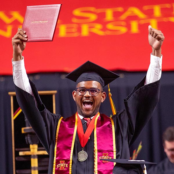 A graduate celebrates receiving his diploma with his hands in the air and a happy shout
