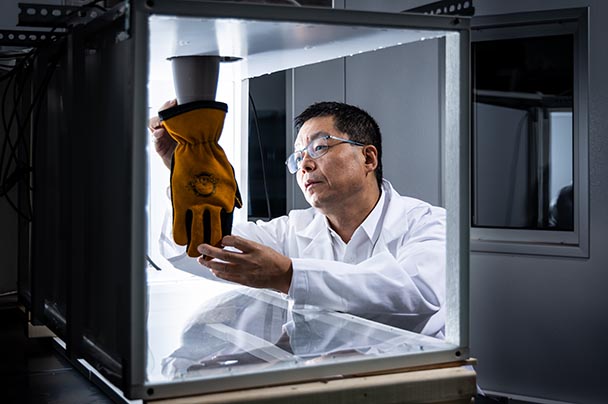 A researcher places a fireman's glove in a lab cube for testing