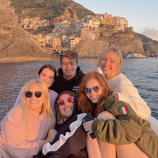 Study abroad students pose on the ocean at sunset