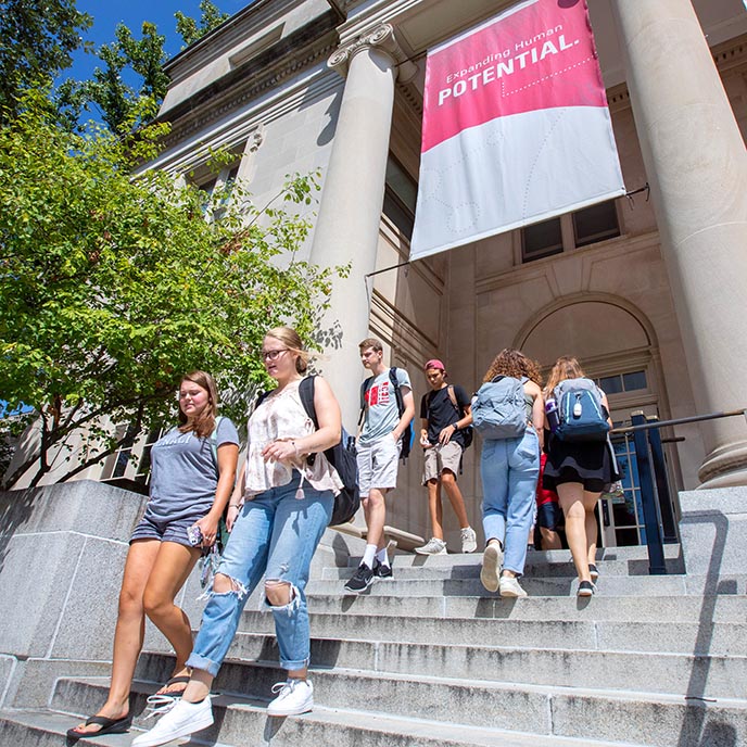 Students exit a campus building on a sunny day