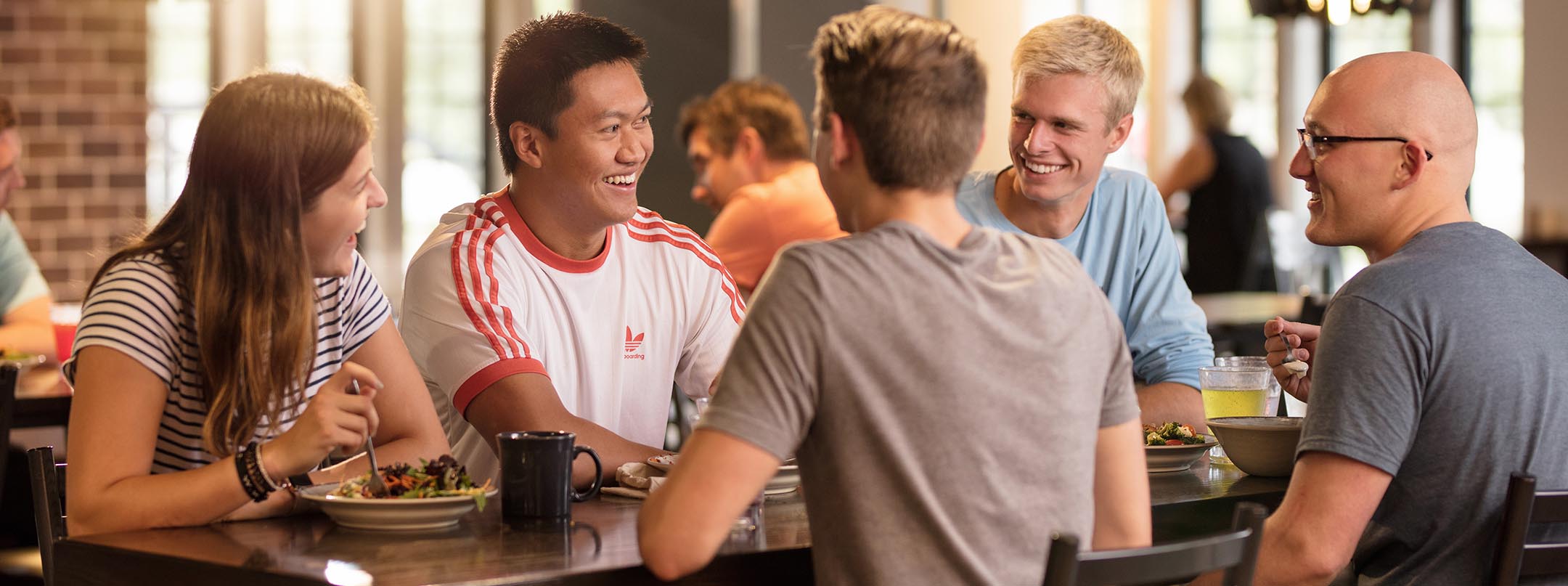 A group of people laugh and talk at a table in a dining center