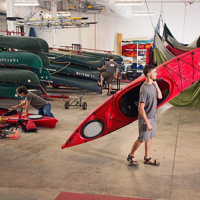 A student carries a kayak from the outdoor rec services supplies