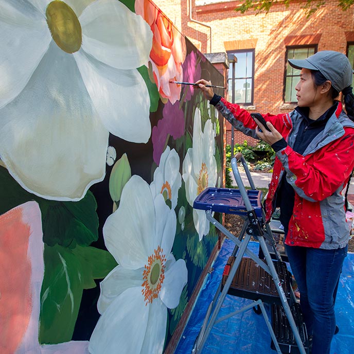 An artist paints a mural on a wall outside The Hub