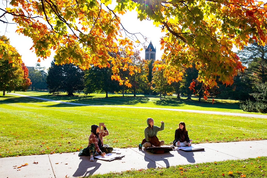 Three students work on a project while seated on central campus on a sunny fall day.