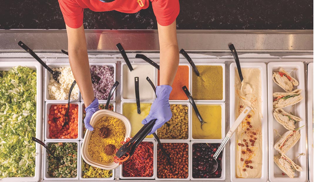 Overhead view of a Dining employee filling the condiment bar.