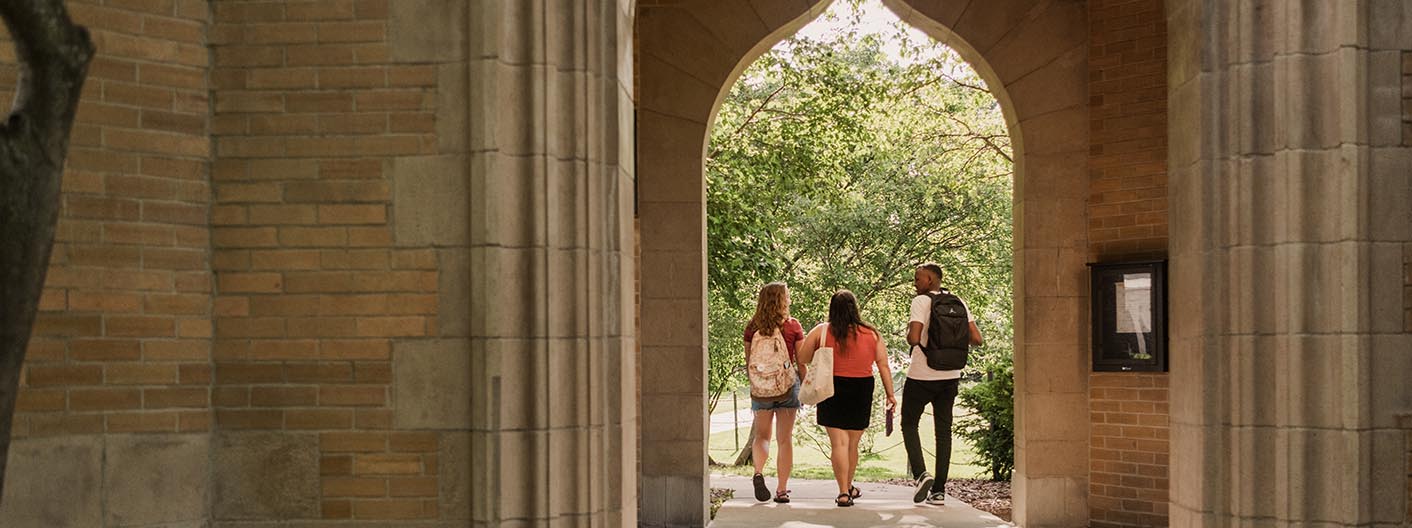 Three students walk through the arch under the campanile.