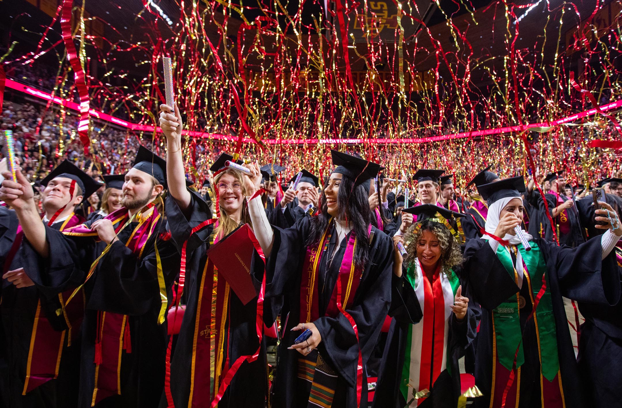 Graduates celebrate at the end of the commencement ceremony as streamers fall from above.