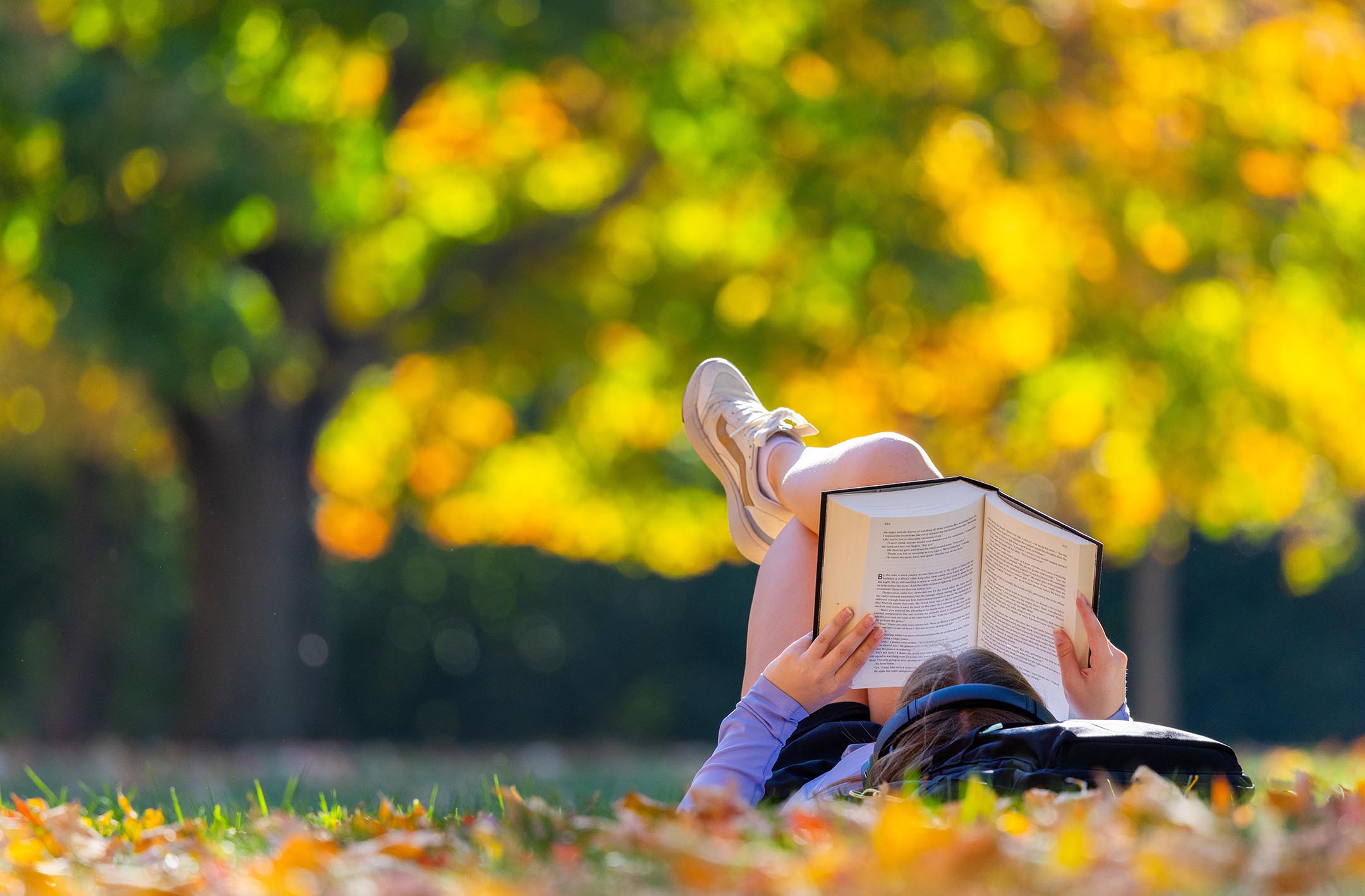 A student reads a book while laying in the sun on central campus.