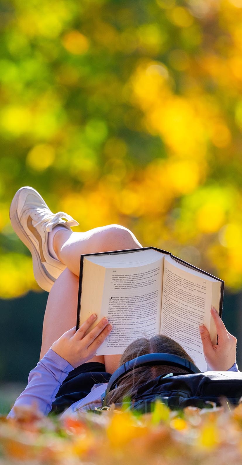 A student reads a book while laying in the sun on central campus.