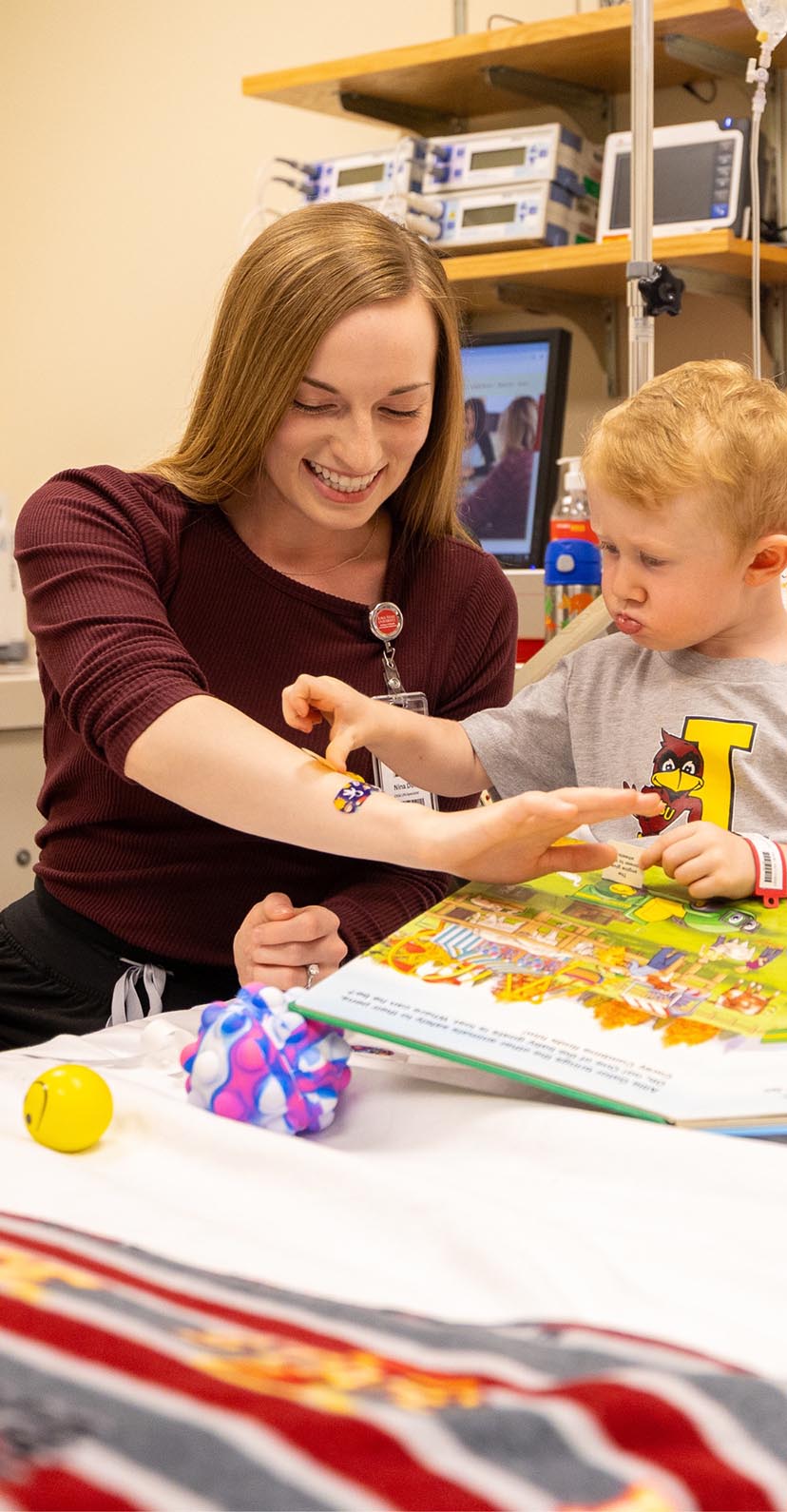 A student plays with a toddler in a hospital bed.