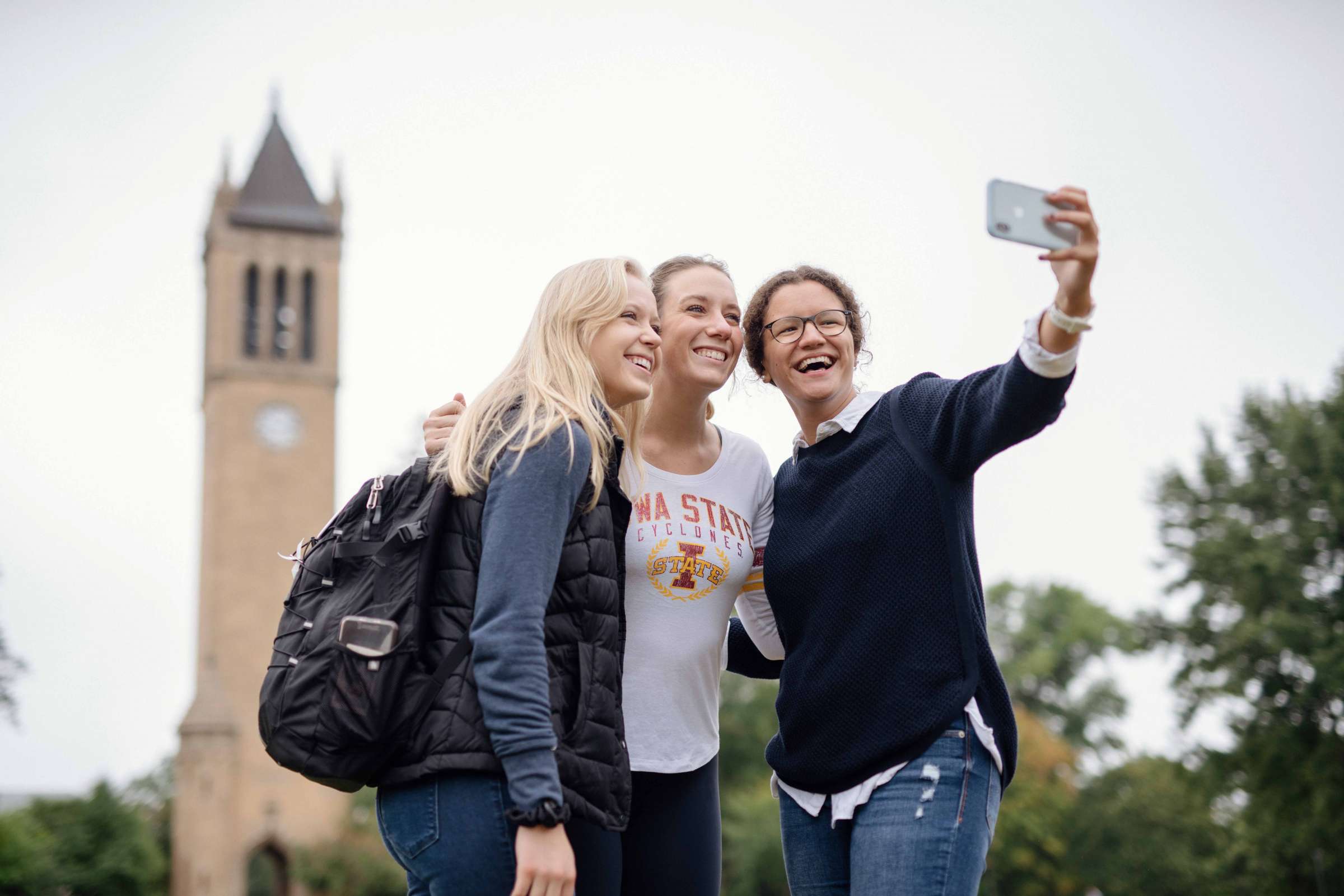 Three students taking a selfie in front of the campanile. 