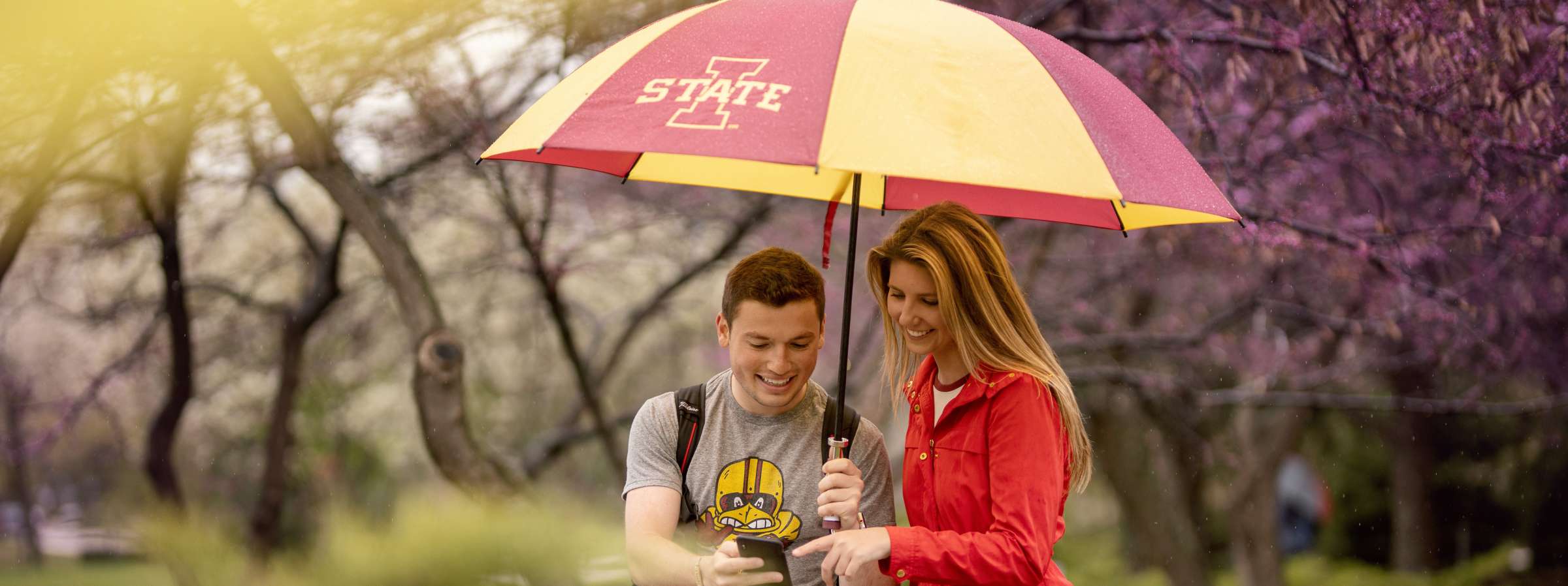 Two students standing under umbrella on campus