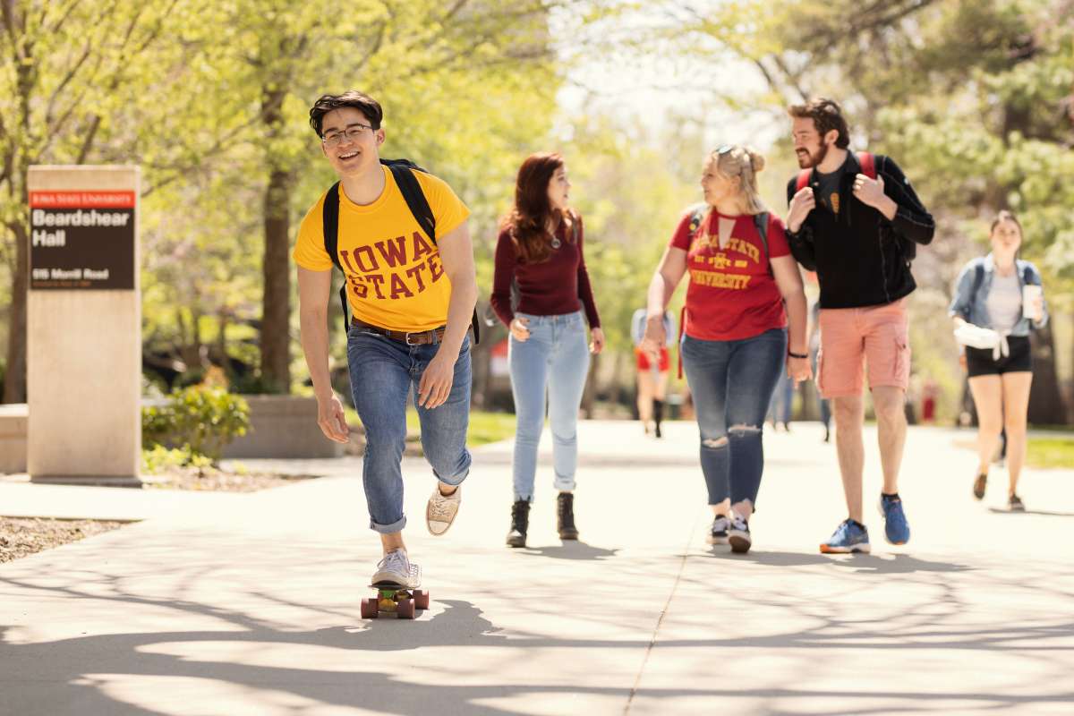 One student skateboarding and three students walking.