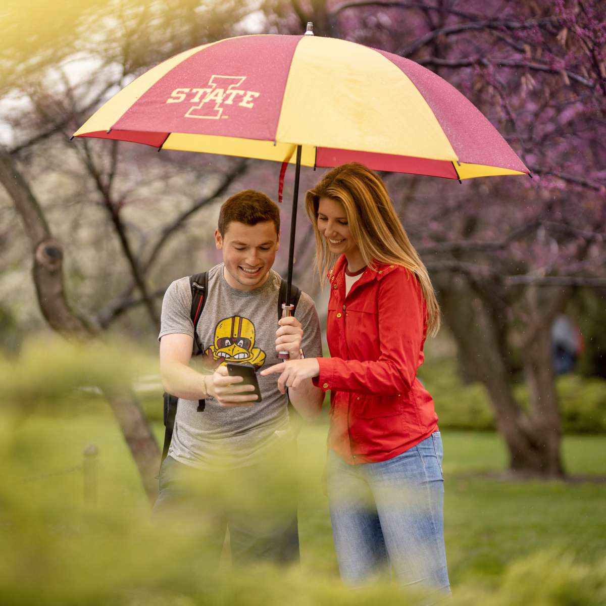 Two students standing under umbrella in the rain. 