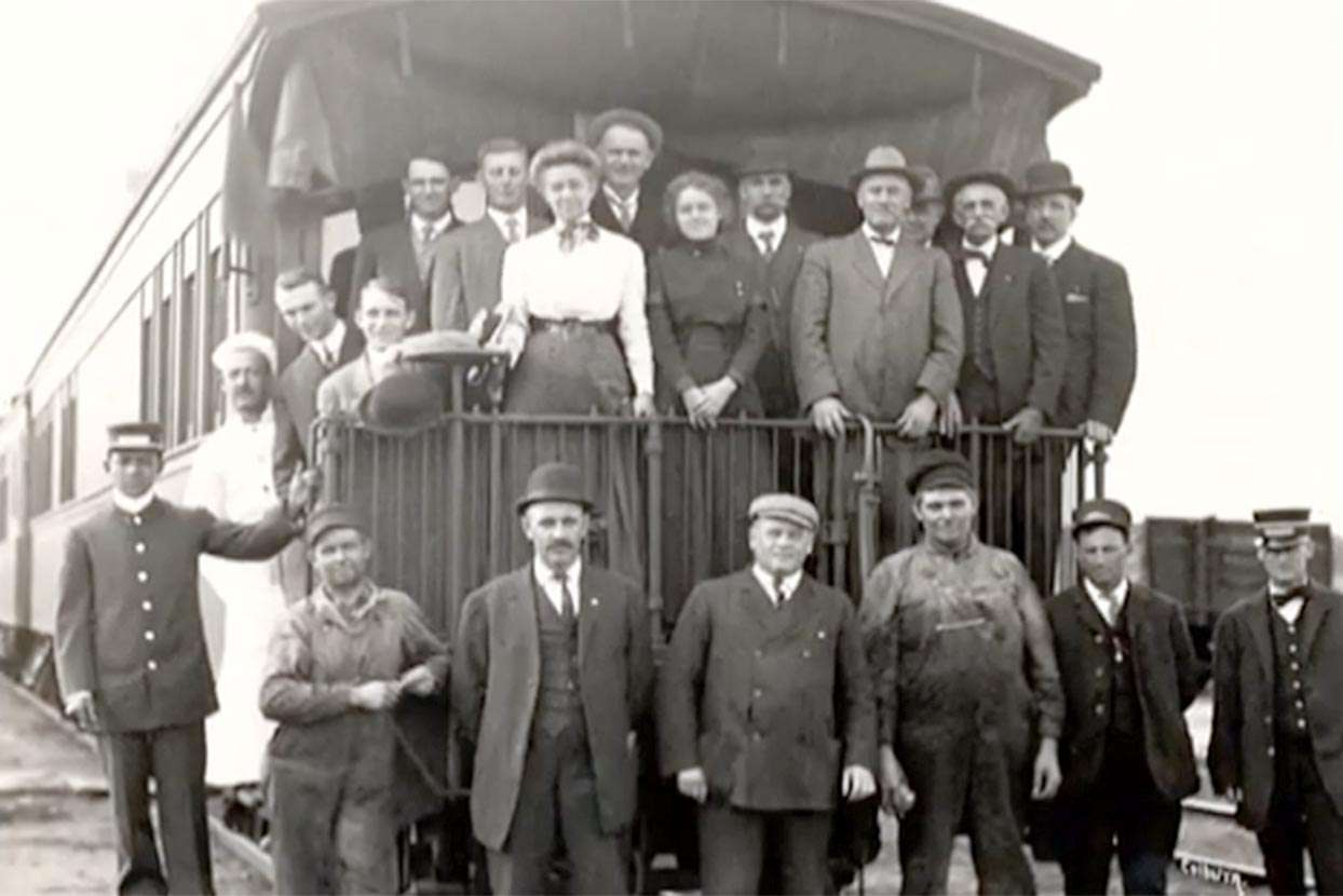 Archived black and white photo of an early traveling extension group posing on the train caboose
